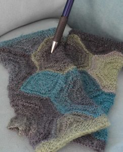 selbstgestrickte Stulpen in Grün-Blautönen mit einem Druckbleistift darauf